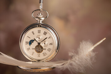 Pocket watch, beautiful pocket watch and a feather, hanging by the chain, abstract background, selective focus.