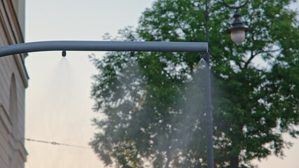 Fototapeta premium Refreshing Water Mist Droplets Spray Curtain Produced By City Street Sprinkler Nozzle for Cooling Pedestrians on Hot Summer Day