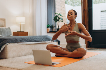 Calm African American woman closing eyes practicing breathing exercises, using laptop at home