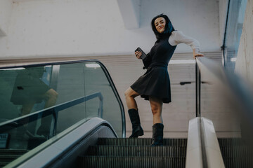 A woman dressed in a fashionable black and white outfit confidently uses an escalator in a contemporary setting. She appears joyful and empowered, exuding a sense of style and confidence.