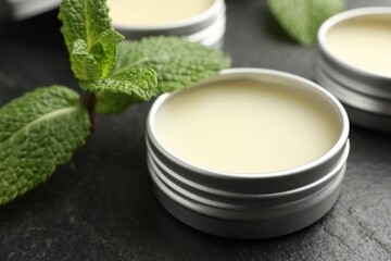 Mint lip balms and green leaves on black table, closeup. Cosmetic product
