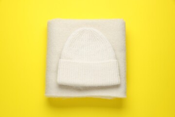 Warm woolen hat and scarf on yellow background, top view