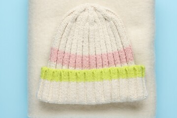 Warm woolen hat and scarf on light blue background, top view