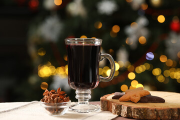 Aromatic mulled wine in glass cup, cookies and anise stars on table against blurred Christmas lights, bokeh effect