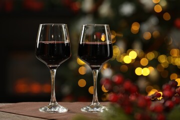 Red wine in glasses on table against blurred Christmas lights, space for text. Bokeh effect