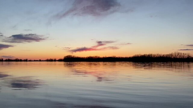 Colorful sunset sky with dark clouds with trees reflection on calm river water 