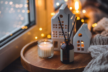 Aroma diffuser, burning candle, Christmas perfume on wooden bamboo tray, knitted sweater. Cozy home decor, hygge and aromatherapy concept. Comfortable atmosphere, Scandinavian decor.