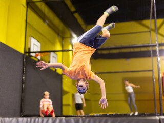 Smiling school-age boy having fun, jumping and indulging on trampolines in entertainment center....
