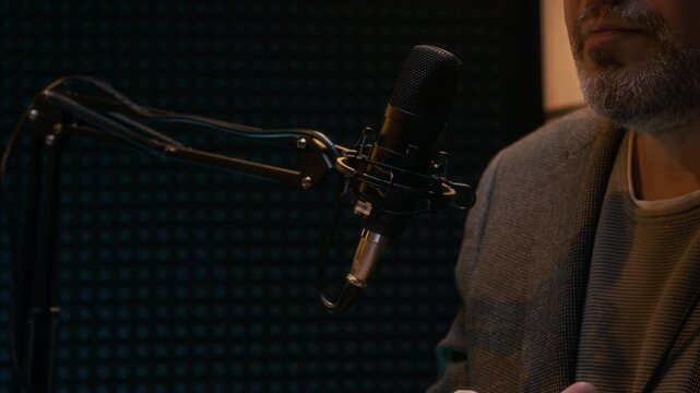 Medium closeup of unrecognizable cheerful mature male podcast guest with grey beard putting on headphones before conducting interview in recording studio and smiling