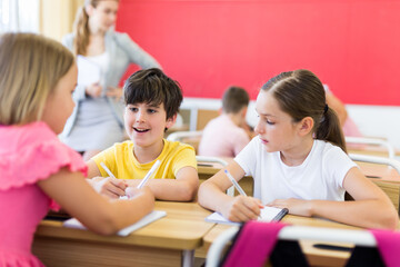 Fototapeta premium Preteen schoolchilds working in groups at lesson in primary school with teacher on background