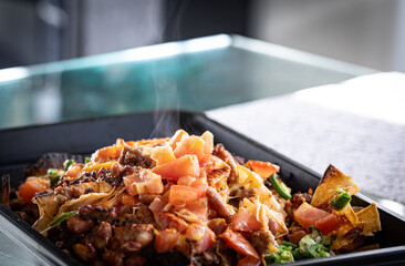 Steaming loaded nachos Mexican dish placed on black metal pan