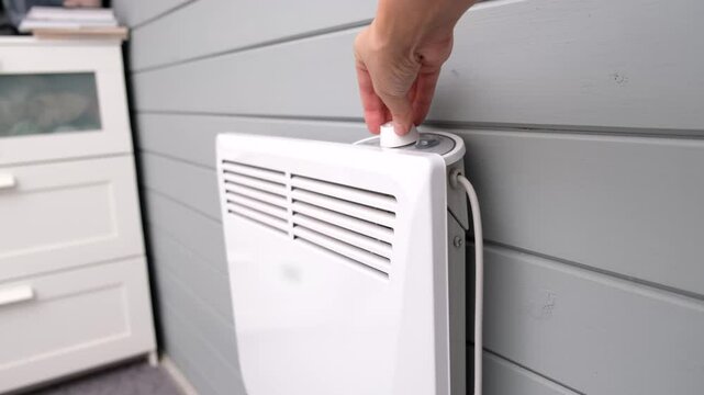 Hand regulating, setting temperature on electric convector, heater thermostate in the room in winter, climate control and energy saving concept