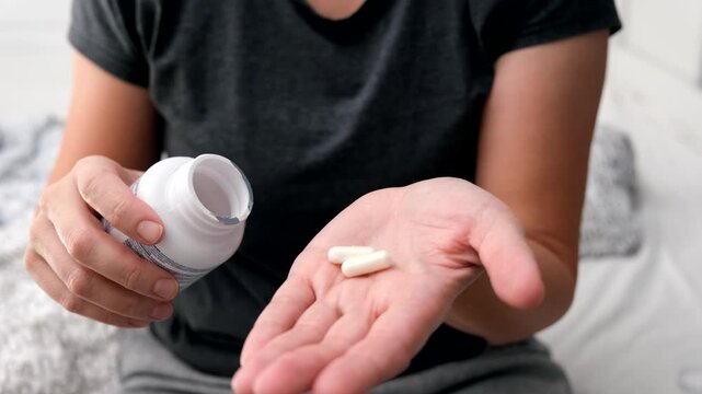 White capsules or Tablets in the hand and on the palm of a girl or woman, close-up. Taking vitamins, painkillers, medications, and dietary supplements.