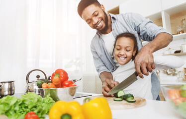 Afro man teaching his little daughter to cut vegetables, cooking salad. Family cooking school...