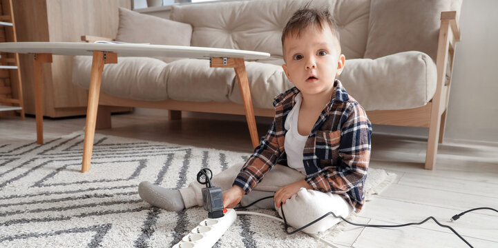 Little boy with plug and extension cord at home. Child in danger