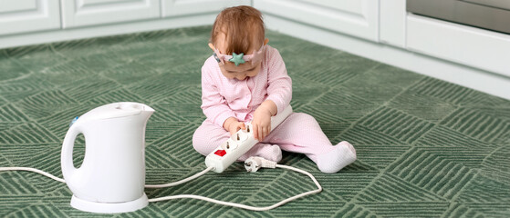 Little baby playing with extension cord and kettle at home. Child in danger