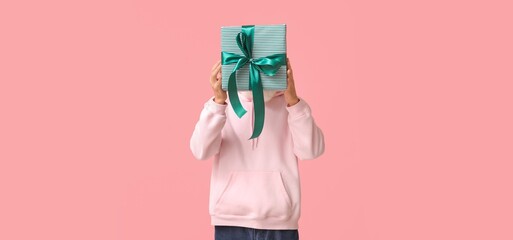 Young man holding Christmas gift on pink background
