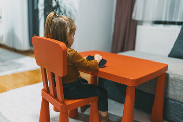 A girl is deeply focused on a smartphone at a compact red table, set in a harmonious and tastefully decorated living room showcasing modern design aesthetics.
