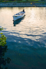 An old style wooden boat is floating on a lake with a red buoy in the water. The boat is small and white with a black stripe. The water is calm and the sky is orange and pink