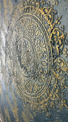 An intricate golden ornamental design embossed on a textured gray surface, featuring floral and geometric patterns. Ideal for luxury design concepts, wallpaper, or decor-related projects.