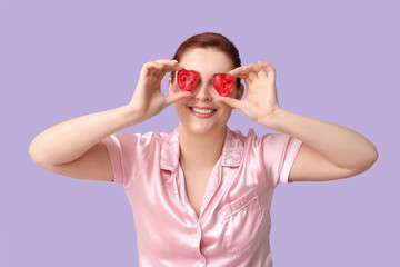 Beautiful young woman covering eyes with heart-shaped soap bars on lilac background