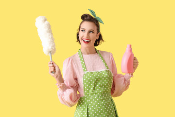 Beautiful young happy pin-up housewife with pp-duster and detergent on yellow background