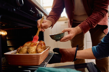Close up of couple preparing roast turkey in oven.