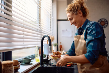 Happy woman washing dishes in kitchen.