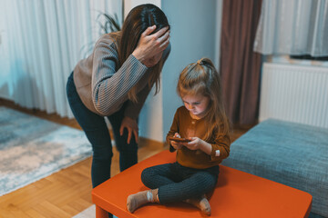 A parent is visibly concerned while a child engages with a smartphone, symbolizing the modern...