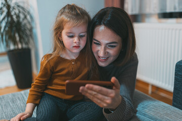 A delightful moment unfolds as a child and adult share a smartphone, emphasizing shared experiences and bonding in tech-friendly home settings in today's era.