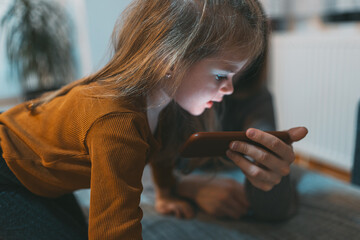 A curious little girl is engrossed in looking at a smartphone screen, reflecting a modern child's...