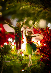 A fairy couple dancing on the Christmas tree whilst balancing on a slender branch. Surroiunded by gold and red tinsel and backlit by festive fairy lights.