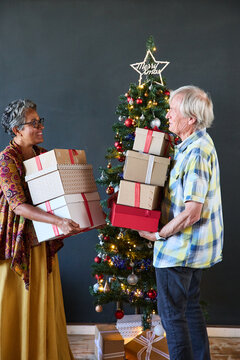Grandparents holding a pile of Christmas presents in a home