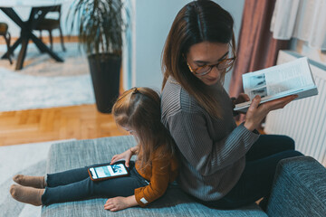 A mother and her daughter are deeply engaged in separate activities, reflecting independence and...