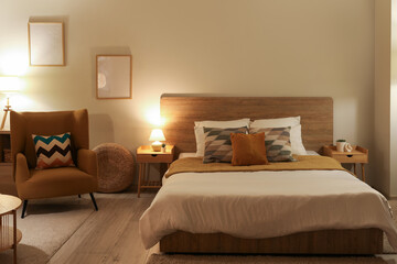 Stylish interior of bedroom with comfortable armchair and bed at evening