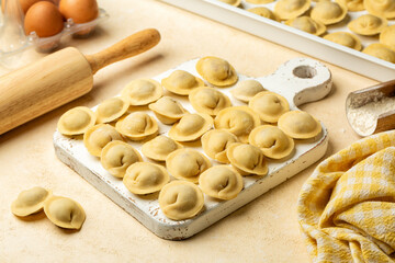 Cooking meat dumplings or pelmeni. Raw unccoked stuffed pasta or ravioli on a white wooden board, flour and egg, dough ingredient.