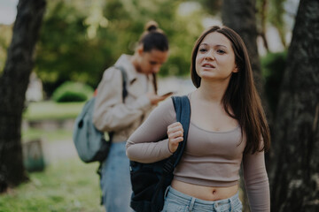 Obraz premium Two young female students walking outdoors with backpacks in a park, enjoying a sunny day and fresh air.