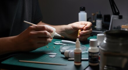 Person assembling small parts at hobby table with tools and glue