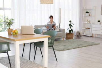 Young woman reading magazine on sofa in dining room