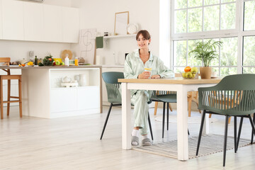 Young woman with glass of lemon water sitting at table in dining room