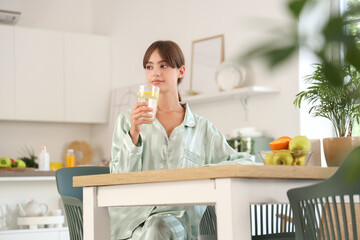 Young woman with glass of lemon water sitting at table in dining room