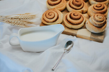 Fresh cinnabons on a wooden tray along with milk and spoon on a white fabric background