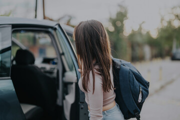 A young girl exits a car wearing a backpack, ready for school on a bright morning. The moment captures the everyday routine of a school drop-off and the anticipation of a new day.