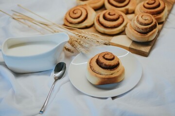 Fresh cinnabon on a plate on a background of other buns on a wooden tray and milk with a spoon 