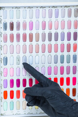 a palette of different nail colors for manicure and a hand pointing at them