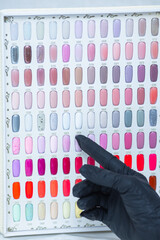 a palette of different nail colors for manicure and a hand pointing at them