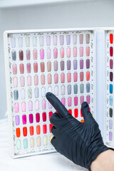 a palette of different nail colors for manicure and a hand pointing at them