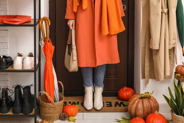 Woman with pumpkins and autumn leaves on doormat in hallway