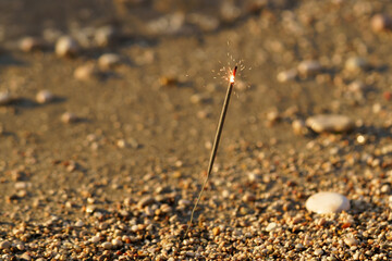 Burning sparkler in sand with pebbles on the beach. Concept of celebration, congratulations. Image for your design