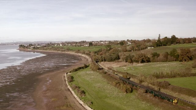 Aerial view of the south coast of England Devon landscape as train travels along the exe river. Drone flying high with rail travel along scenic landscape UK 4K